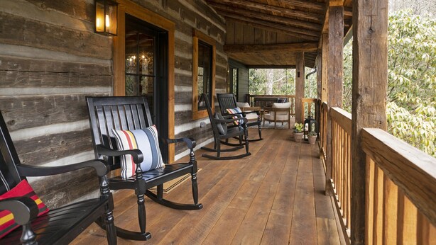 A log cabin with a wooden porch, rocking chairs, and a table. - The Kingfisher: Flat Mountain Farm (Highlands)