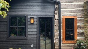 A log cabin with a dark exterior, two front doors, a small porch with potted plants, and a stone foundation. - The Kingfisher: Flat Mountain Farm (Highlands)
