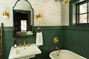 A bathroom with a white sink, a bathtub, a mirror, and green walls.