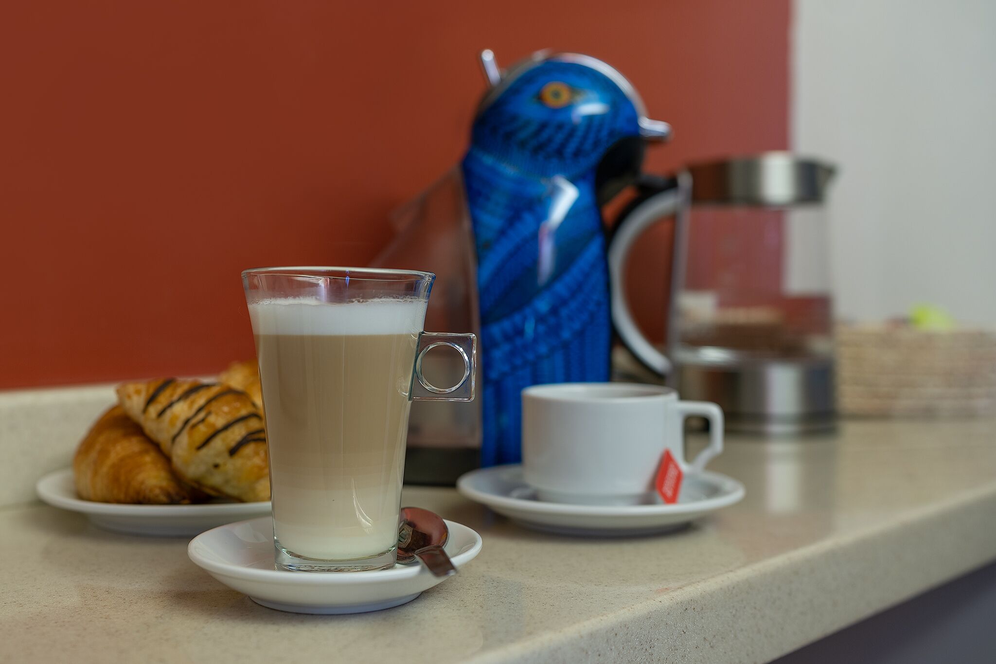 A table with a glass of milk, a croissant, a teapot, and a cup.