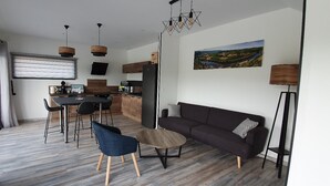 Een moderne woonkamer met een donkere bank, een ronde salontafel en een eethoek met een zwarte tafel en stoelen.