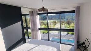 Een slaapkamer met een groot raam, een bed en uitzicht op een zwembad en groen.