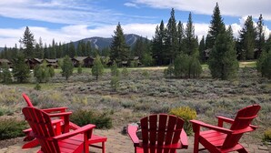 Eine Terrasse mit roten Adirondack-Stühlen und einem Tisch, mit Blick auf eine gebirgige Landschaft und ein Hotel im Hintergrund.