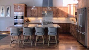 Eine moderne Küche mit Holzausstattung, einem Edelstahlkühlschrank und einer zentralen Kochinsel mit Barhocker.