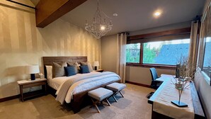 Ein Schlafzimmer mit einem großen Bett, Nachttischen, einer Bank, einem Schreibtisch und einem Fenster mit Blick.