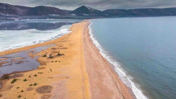 Eine Küstenlandschaft mit Sandstrand, ruhiger See und fernen Bergen unter bewölktem Himmel.