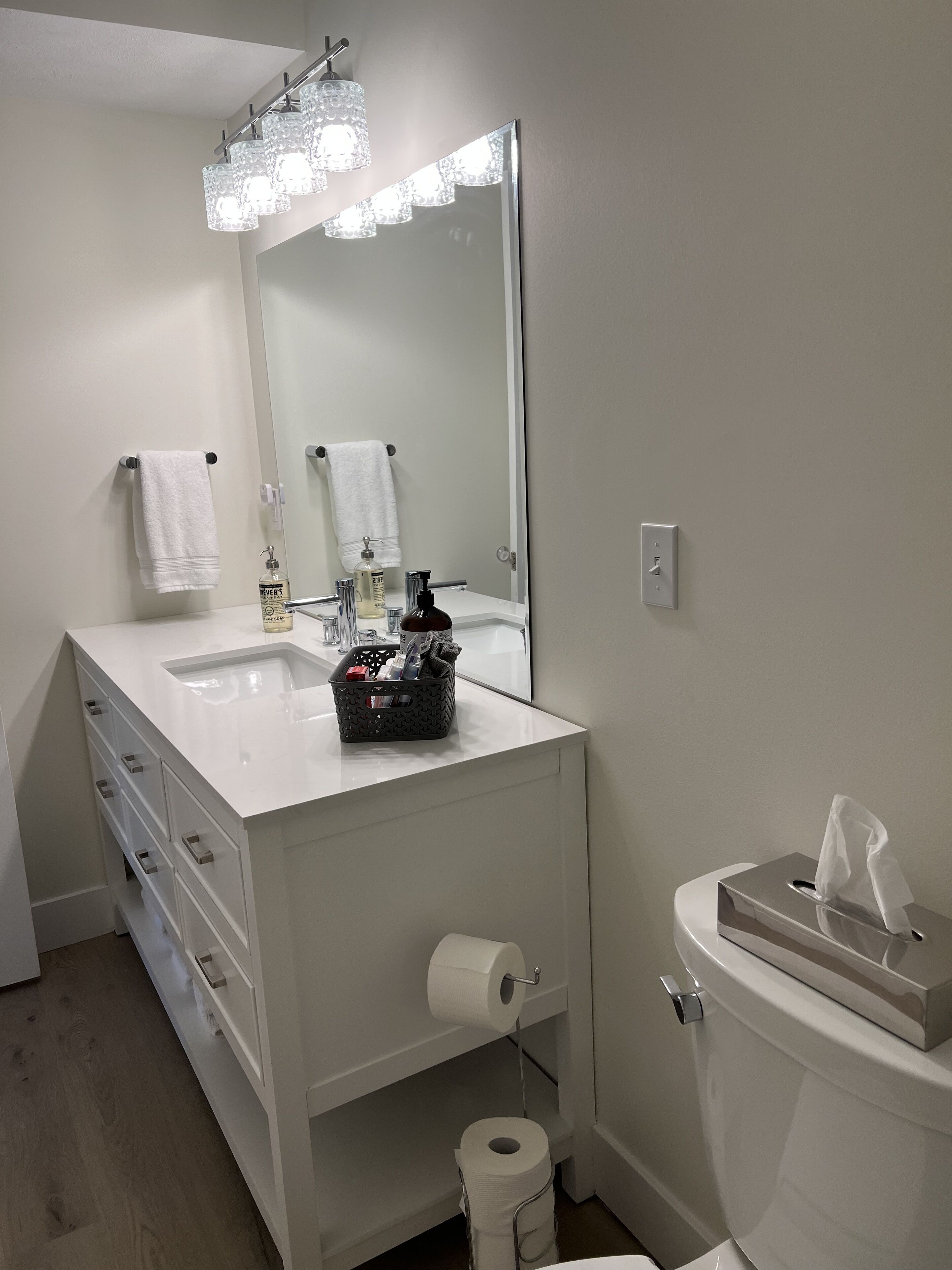 A modern bathroom with a white vanity, a large mirror, a toilet, and a tissue box.
