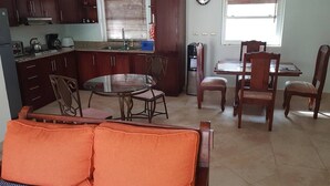 Una cucina funzionale con zona pranzo, che comprende un tavolo rotondo e sedie, un divano con cuscini arancioni e un frigorifero.