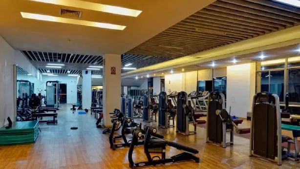 A spacious gym with various exercise machines, wooden flooring, and a modern ceiling design. - Century City Badminton Club Hotel (Dongguan)