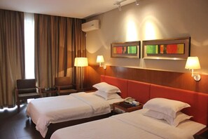 A hotel room with two beds, a chair, a nightstand, and two wall-mounted lamps.