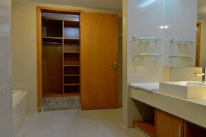 A bathroom with a white sink, a mirror, and a wooden door leading to a closet.