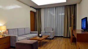 A modern hotel room with a sofa, armchair, ottoman, wooden coffee table, and a TV on a wooden stand. - Century City Badminton Club Hotel (Dongguan)