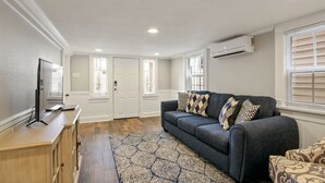 Un soggiorno con un divano grigio scuro, cuscini decorati, un tavolino in legno e un televisore.