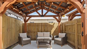 Una zona patio coperta con tre poltrone in vimini e un tavolo centrale, circondata da recinzioni in legno.