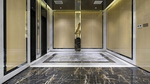 An elevator interior with marble flooring, glass doors, and a central decorative element. - Huangcheng Imperial Garden Hotel (Hefei)