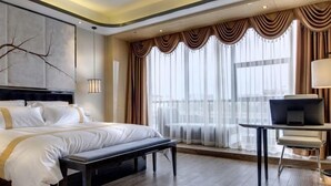 A modern hotel room with a large bed, a bench, a desk, and a view of the city through sheer curtains. - Huangcheng Imperial Garden Hotel (Hefei)