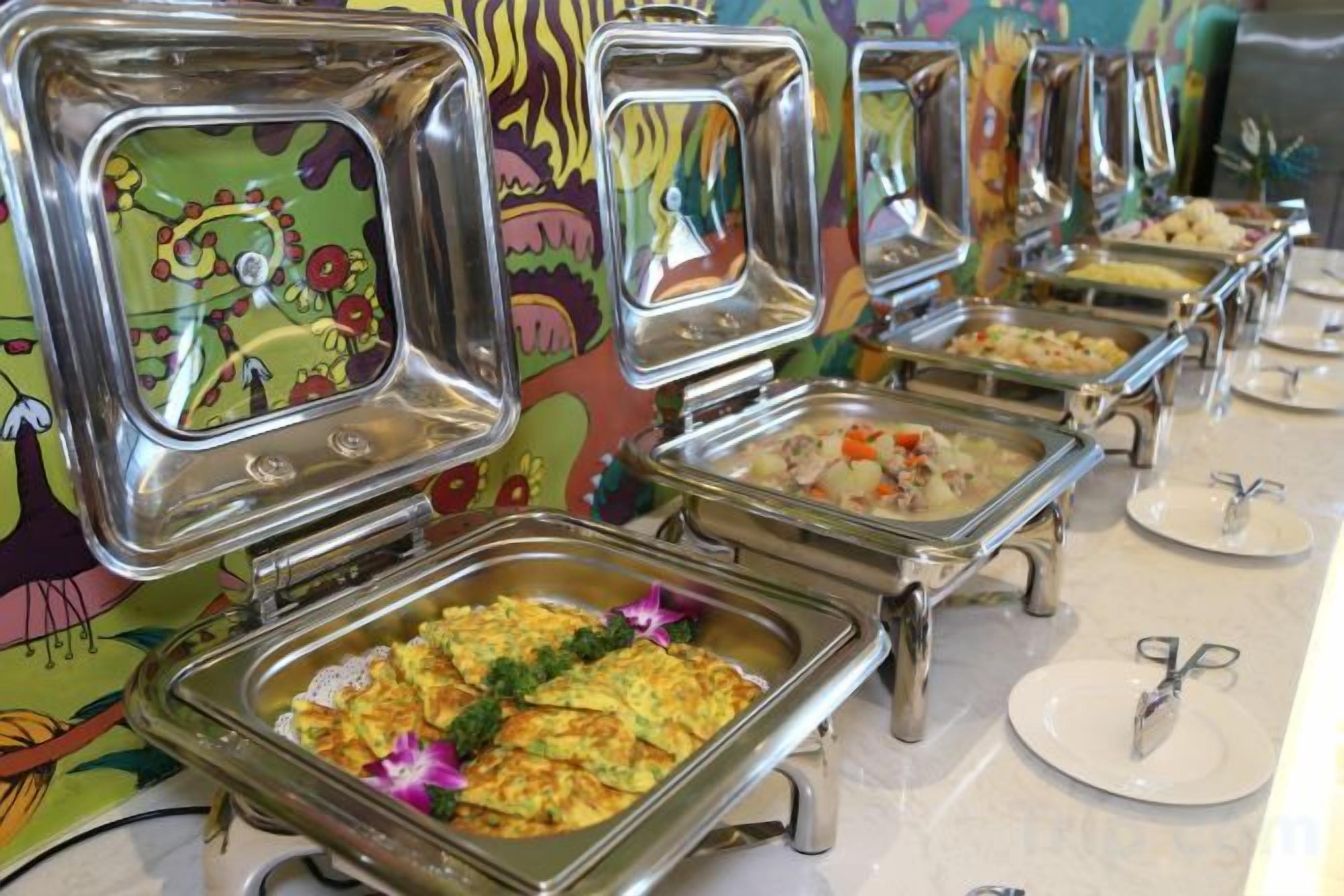 Un bufé con varias estaciones de servicio, cada una con una bandeja metálica y un plato.