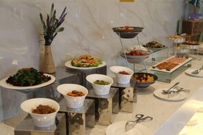 A buffet with various dishes and a vase of purple flowers. - Jujian Hotel (Harbin)