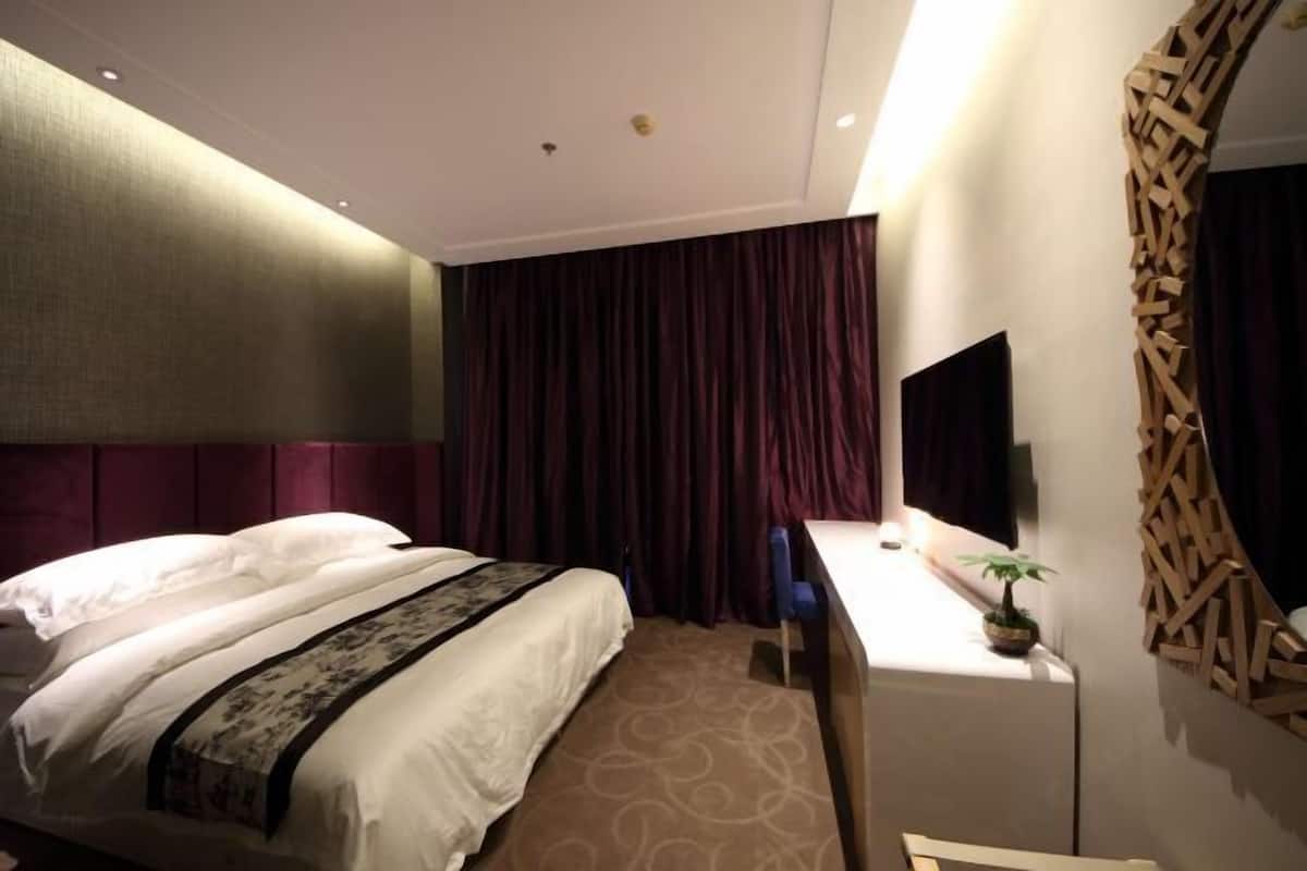 A hotel room with a bed, a desk, a television, and a decorative wall panel.