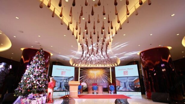 A lobby with a Christmas tree, a stage with a backdrop, and hanging light fixtures. - Jujian Hotel (Harbin)