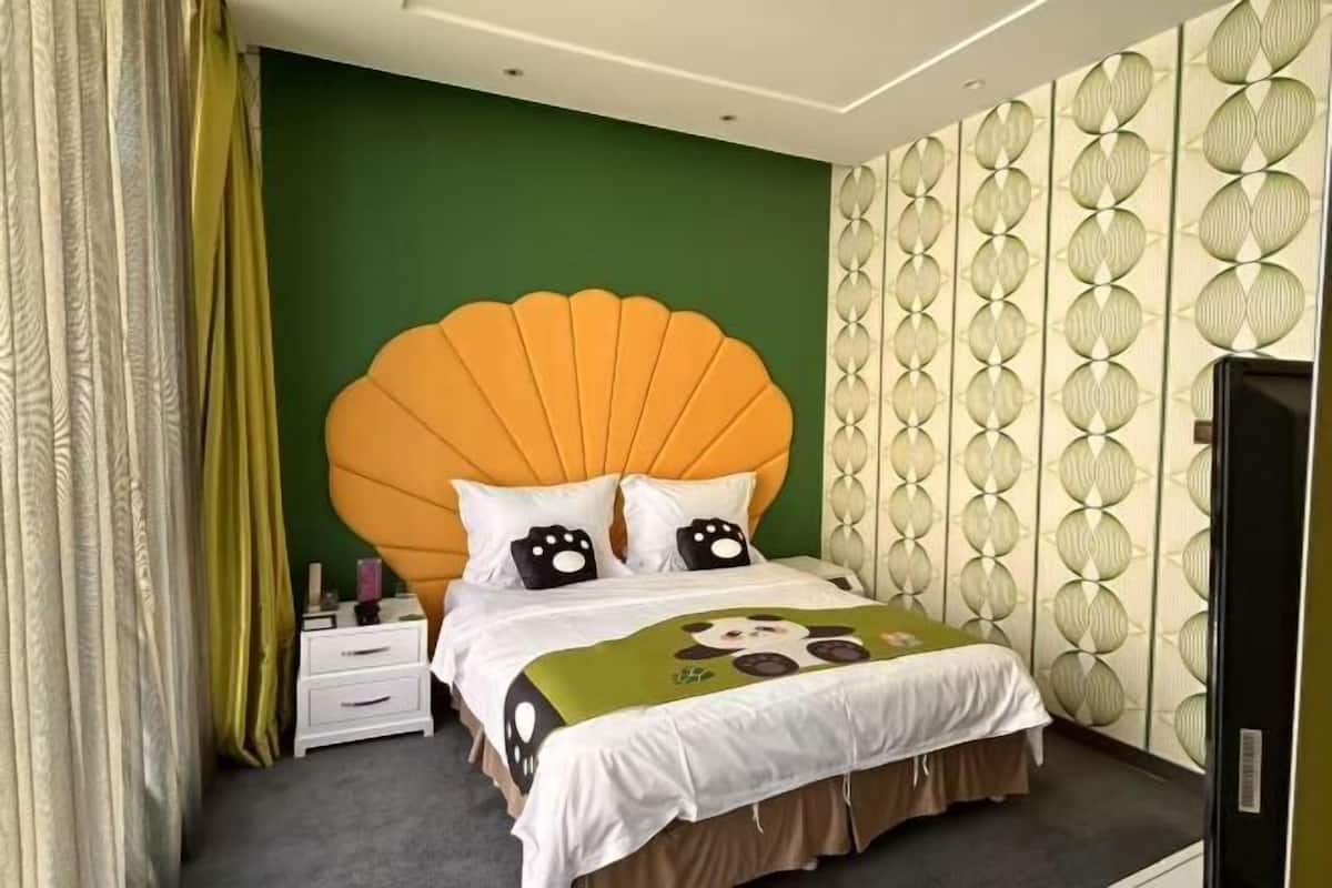 A hotel room with a large orange headboard, a green accent wall, and a patterned wallpaper.