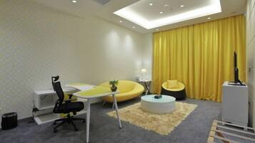 Un salon moderne avec un canapé jaune, une table basse ronde, un fauteuil de bureau noir et une petite plante.