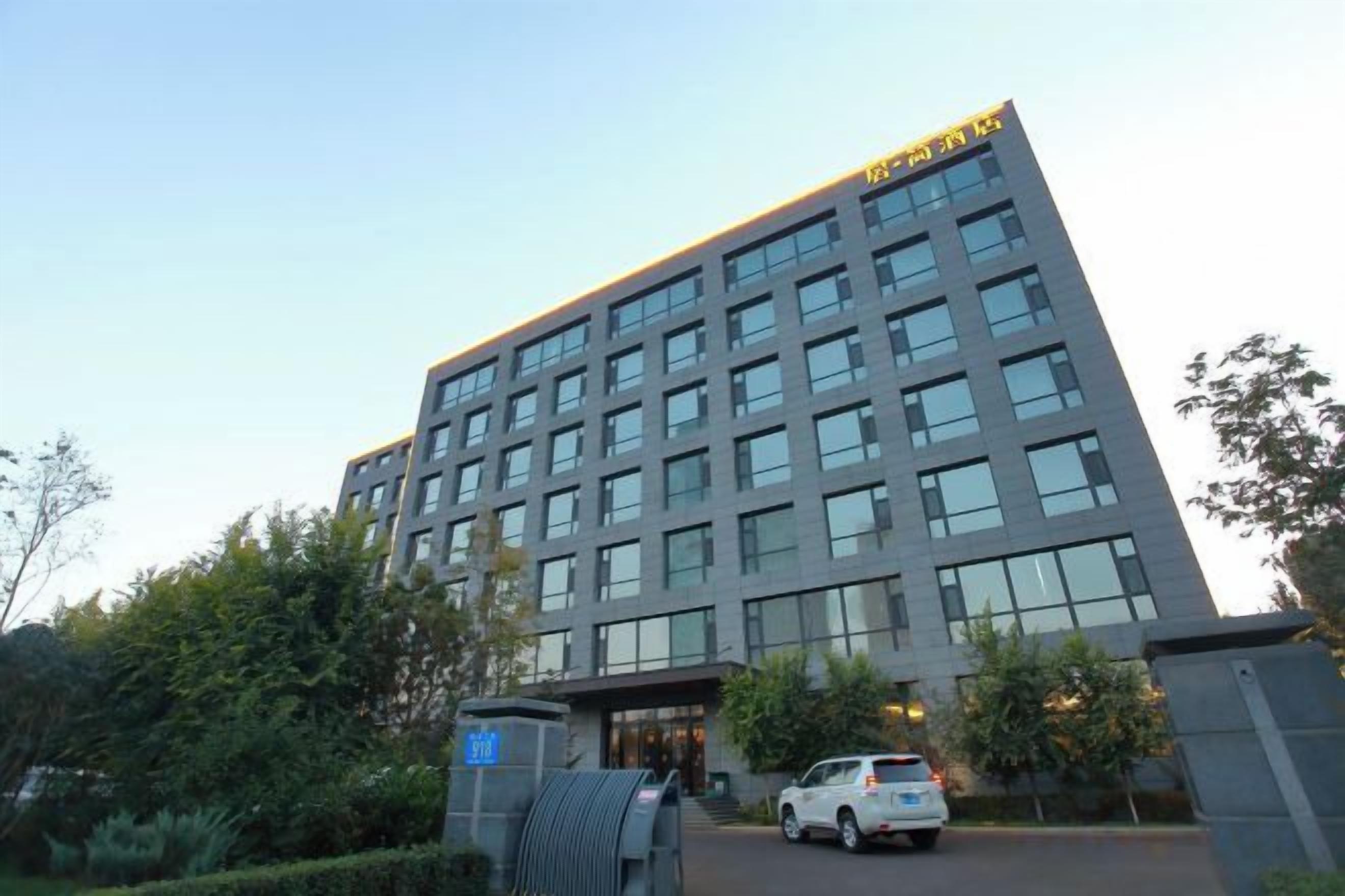 Um edifício moderno de vários andares, com design arquitetônico marcante, entrada imponente e área de estacionamento com veículos.