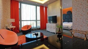A modern hotel room with a flat-screen TV, a bed, a sofa, a coffee table, and a large window with curtains. - Jujian Hotel (Harbin)