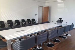 Un salón de conferencias con una larga mesa y varias sillas, una puerta y una pizarra.
