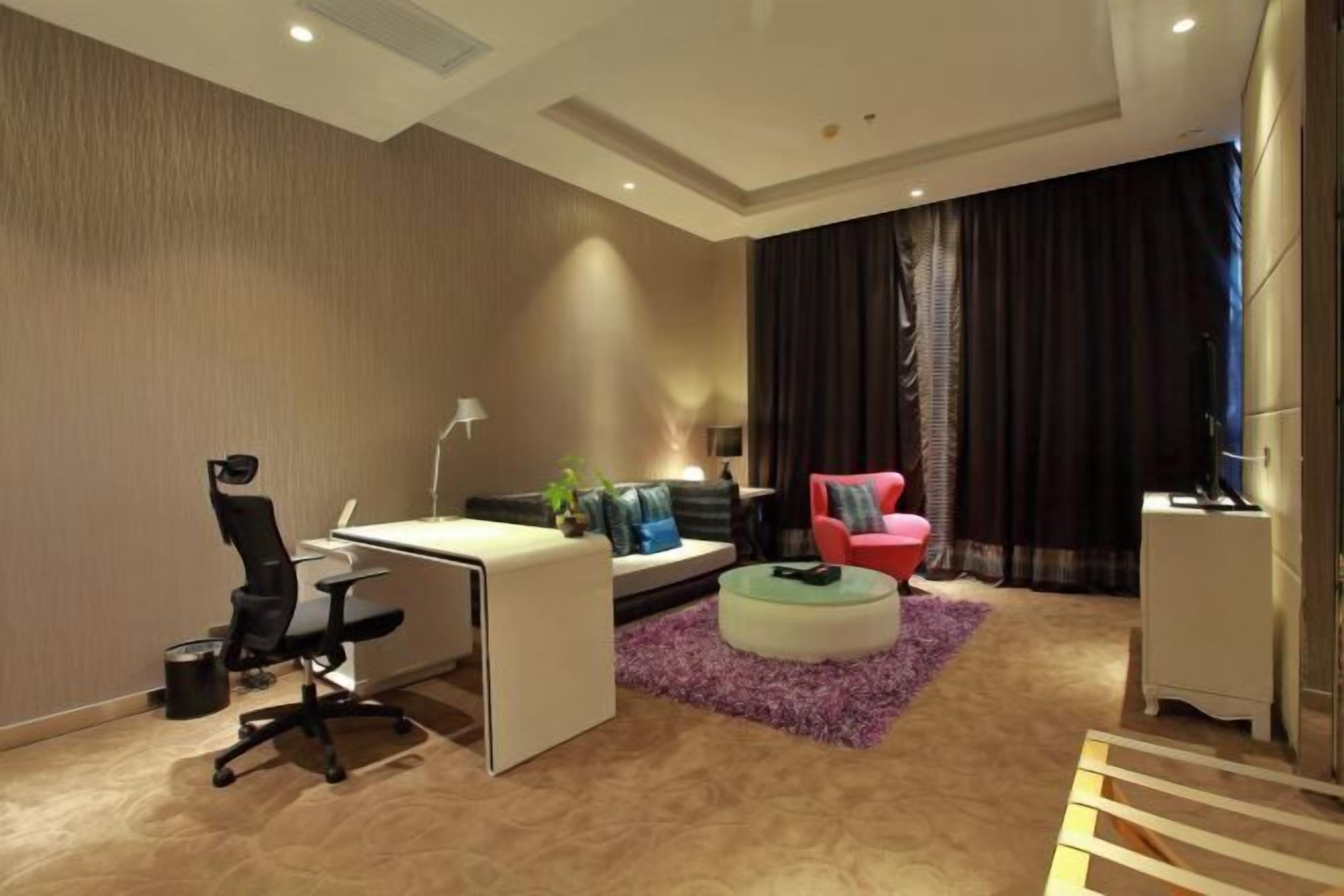 Un salon moderne avec un bureau, un fauteuil rouge, un canapé et une grande fenêtre avec des rideaux.