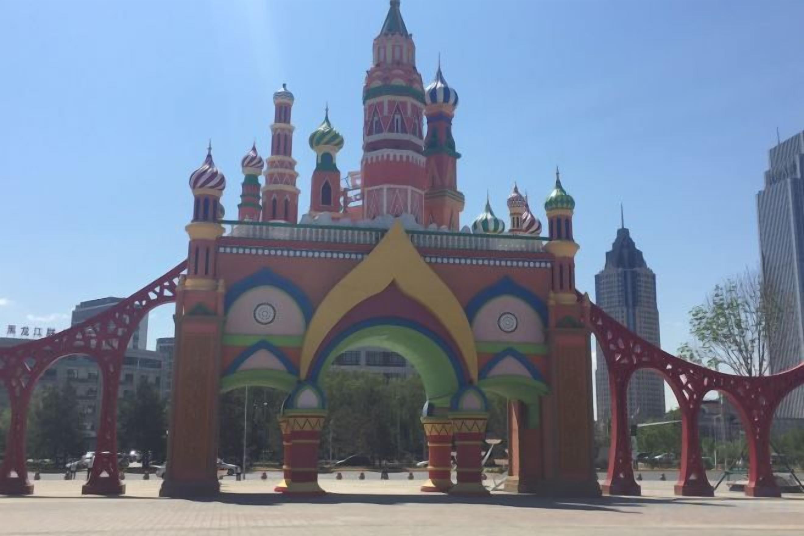 A colorful building with multiple domes and arches, surrounded by modern skyscrapers.