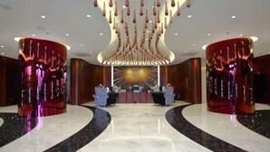 A lobby with a central reception desk, two large cylindrical columns, and a ceiling with hanging light fixtures. - Jujian Hotel (Harbin)