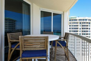 Ein Balkon mit rundem Tisch und vier Holzstühlen, großen Fenstern und Blick auf ein Hotelgebäude.