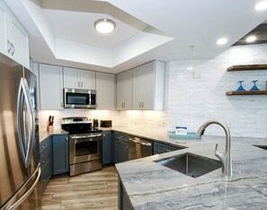 A modern kitchen with stainless steel appliances, a marble countertop, and a built-in oven.