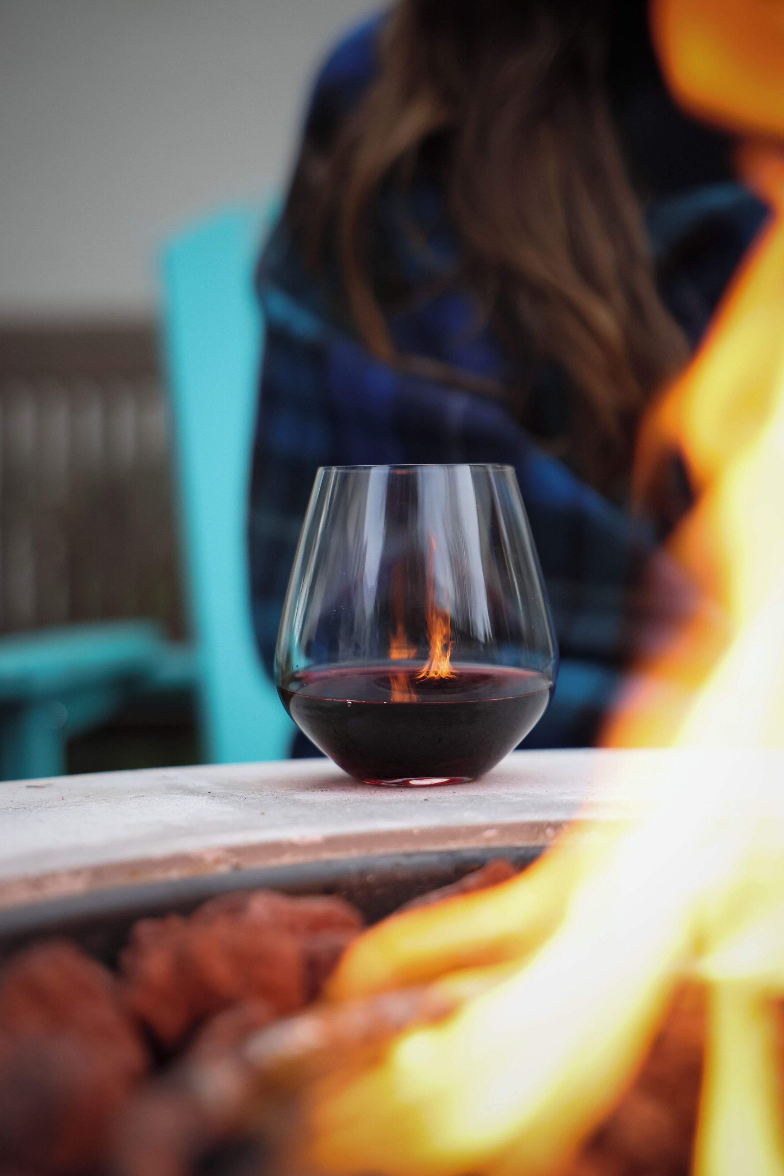 A glass of red wine on a table with a fire in the foreground.