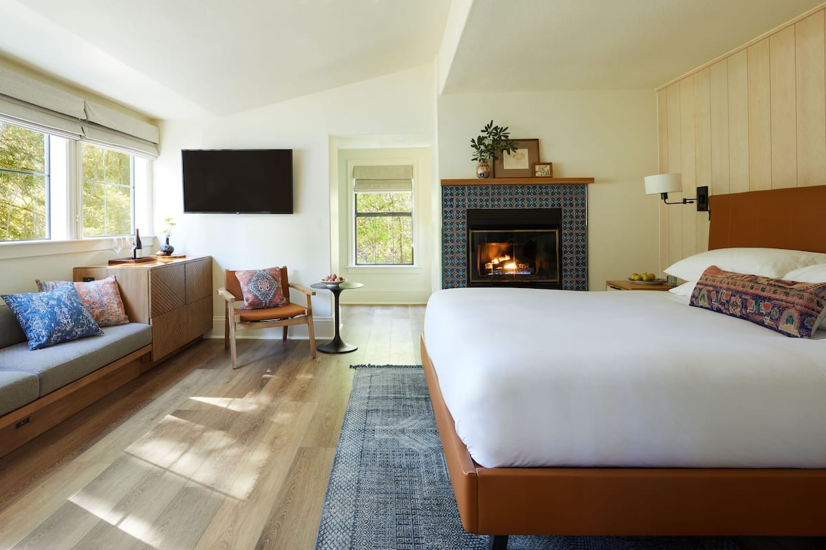 Un dormitorio con una cama grande, un sofá, una silla, una chimenea y un televisor en la pared.