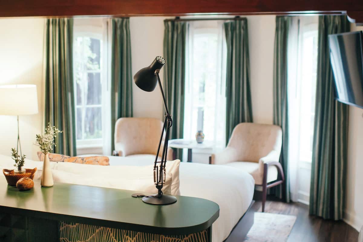 Una habitación de hotel con una cama, un escritorio con lámpara, una silla y un televisor.