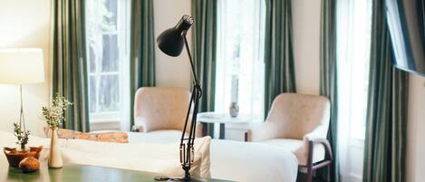 A hotel room with a bed, a desk with a lamp, a chair, and a TV.
