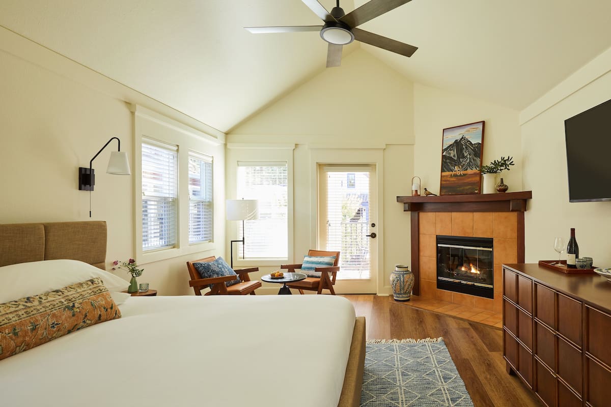 Un dormitorio con una cama grande, chimenea, ventilador de techo y comedor con sillas y mesa.