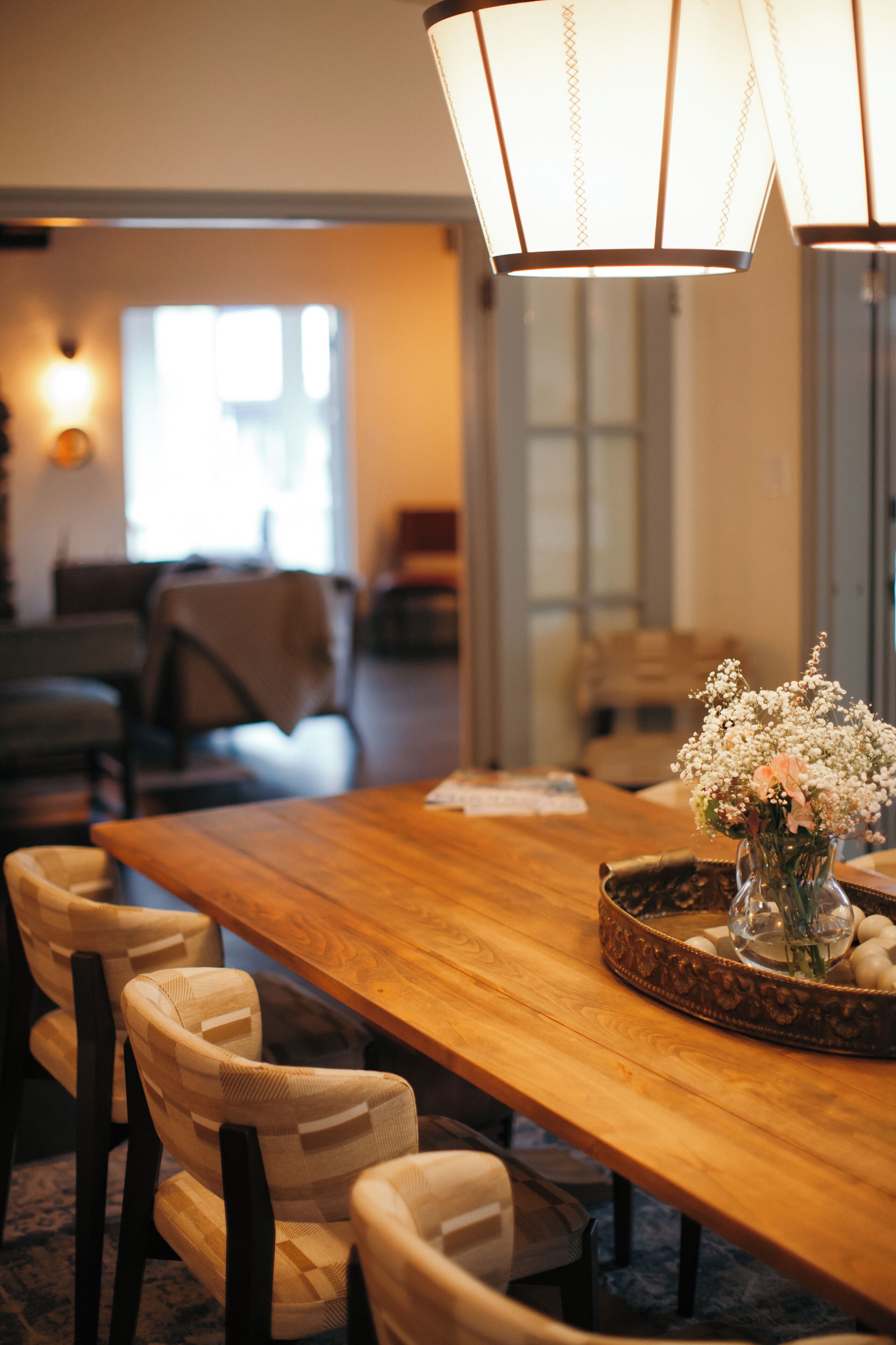 A wooden dining table with a vase of flowers, chairs, and a lamp.