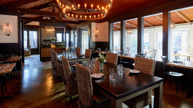 Un vaste espace dédié à la salle à manger, avec une grande table en bois, des chaises en osier et un lustre circulaire.