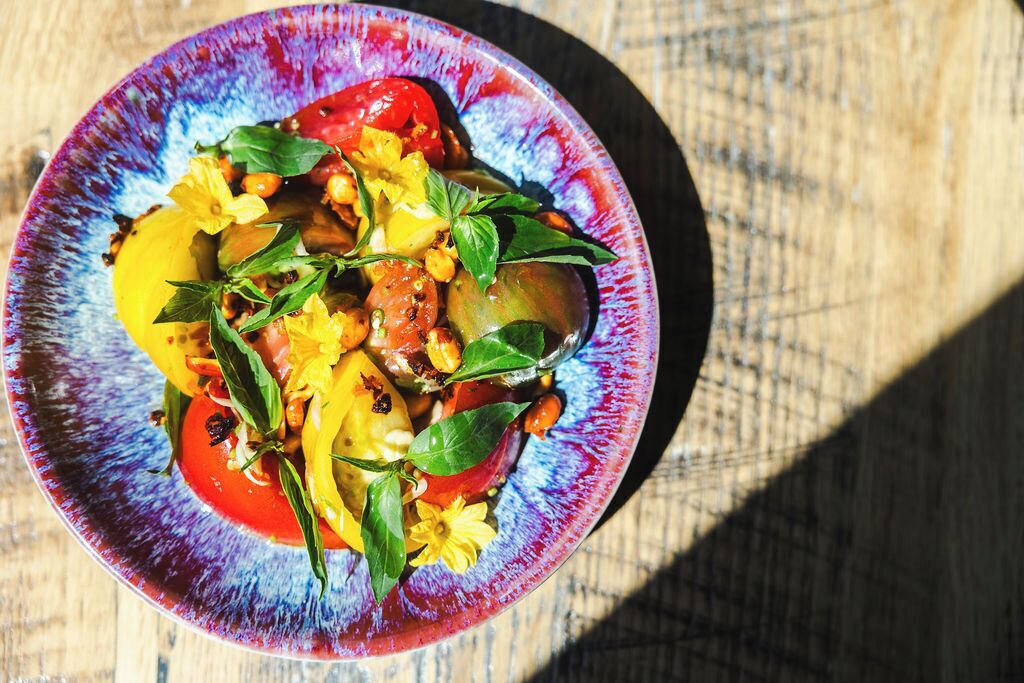 Un tazón colorido de ensalada con tomates, pimientos amarillos y hierbas sobre una mesa de madera.