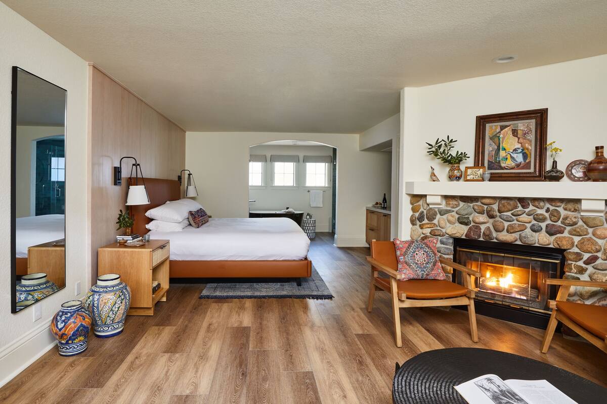 Un dormitorio moderno con una cama grande, mesitas de noche, una chimenea y vistas al pasillo.