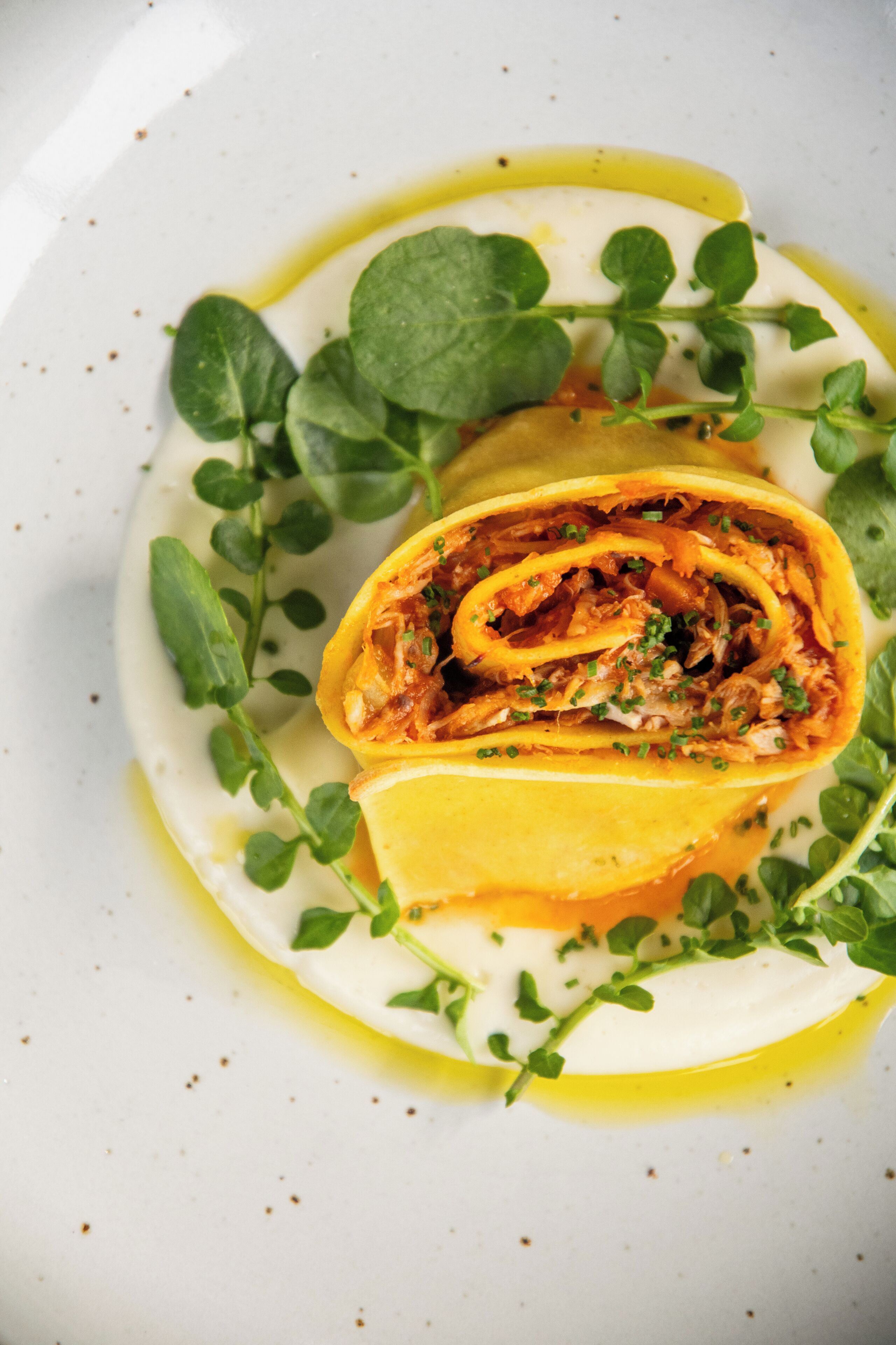 A plate with a rolled dish, garnished with green leaves and a yellow sauce.