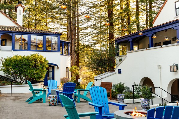 Un espacio de estar al aire libre con sillas Adirondack azules, una chimenea y plantas en macetas.