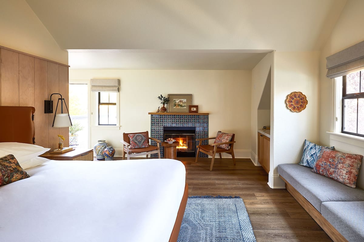 Un dormitorio amplio con una cama grande, un sofá, dos sillones, una chimenea y vistas al exterior.
