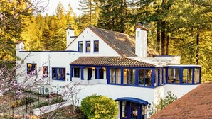 Un bâtiment blanc avec des bordures bleues et un toit recouvert de tuiles, entouré d’arbres.