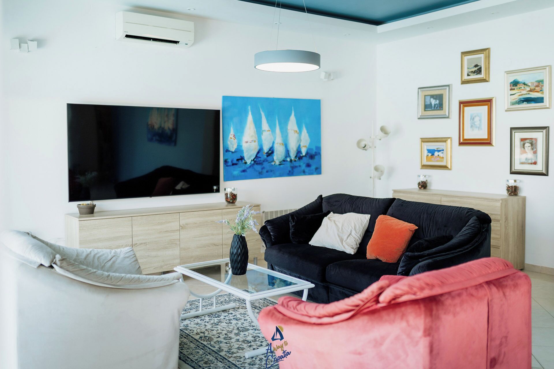 A living room with a flat-screen TV, a black sofa, a glass coffee table, and a patterned rug.