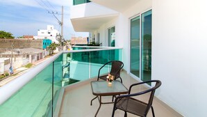 A balcony with a glass railing, two wicker chairs, and a small table with a vase of flowers. - Hotel Playa Norte (Cartagena)