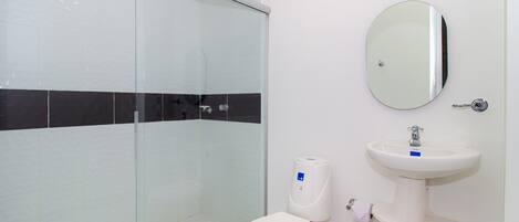 A bathroom with a glass shower enclosure, a white toilet, a pedestal sink, and a round mirror.